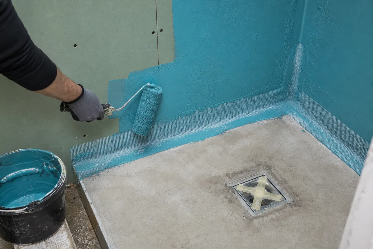 Application au rouleau d&rsquo;un système d&rsquo;étanchéité sous carrelage bleu sur les murs d&rsquo;une douche