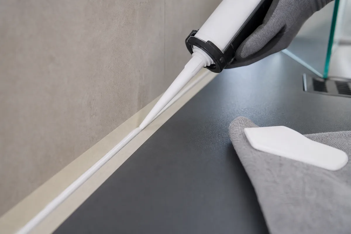 Détail d&rsquo;un joint silicone appliqué au pistolet entre un receveur de douche et un carrelage mural